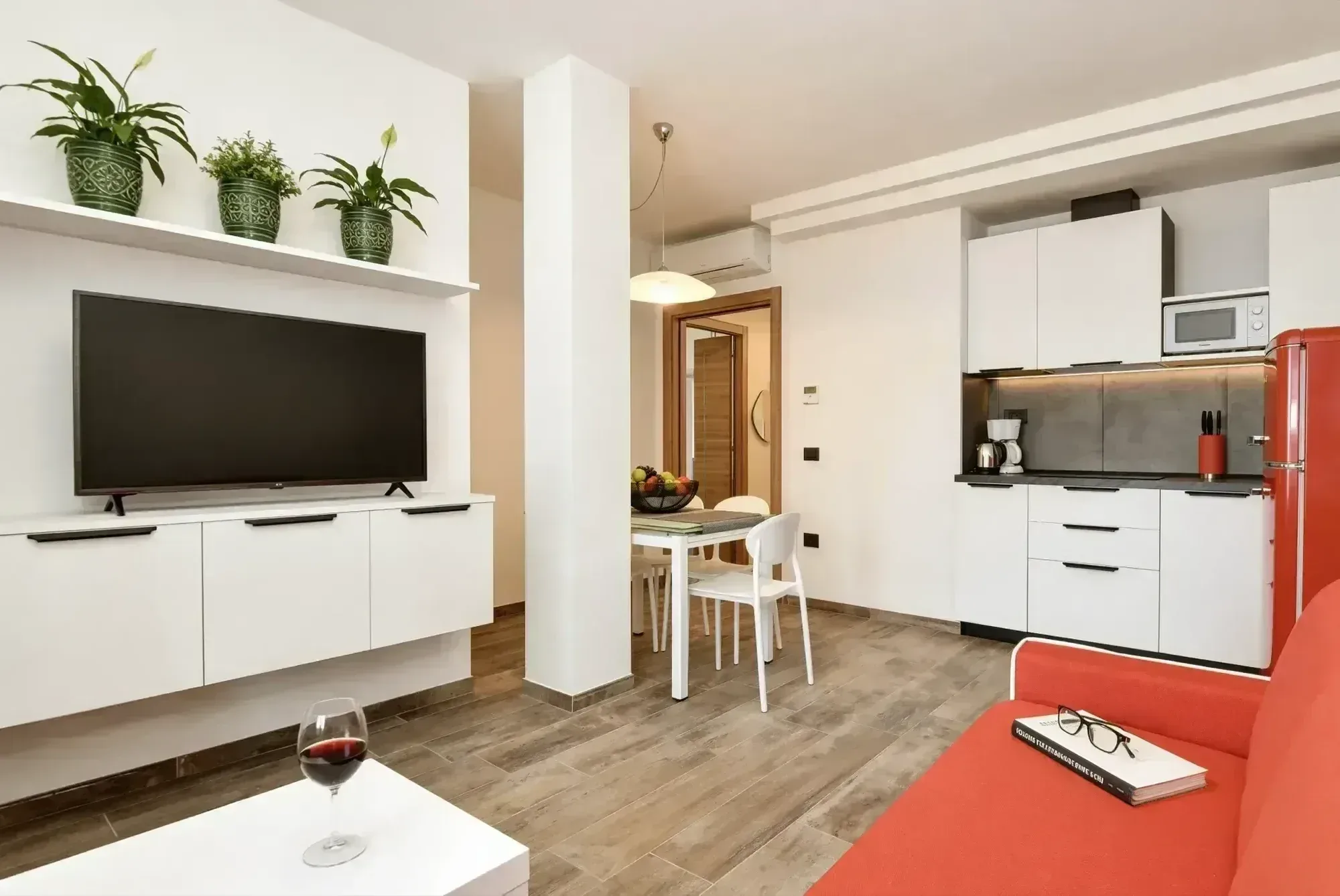 Soggiorno con angolo cottura, frigo rosso, TV e divano, appartamento al Lago di Garda