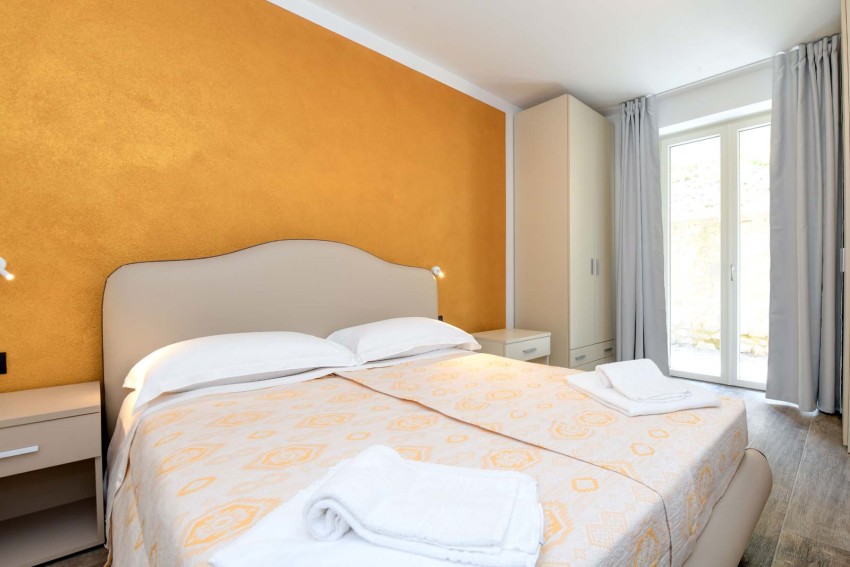 Helles Doppelzimmer mit orangefarbener Akzentwand und Handtüchern, Lago di Garda
