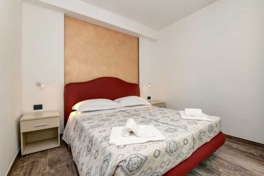 Modern double bedroom with red headboard and towels near Lago di Garda