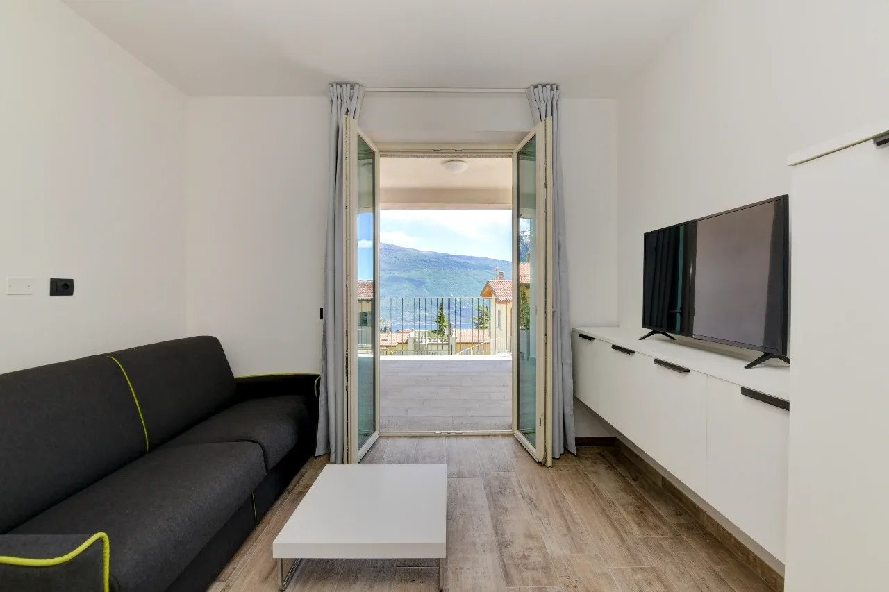 Modernes Wohnzimmer mit TV und Sofa, Balkon mit Blick auf den Lago di Garda.