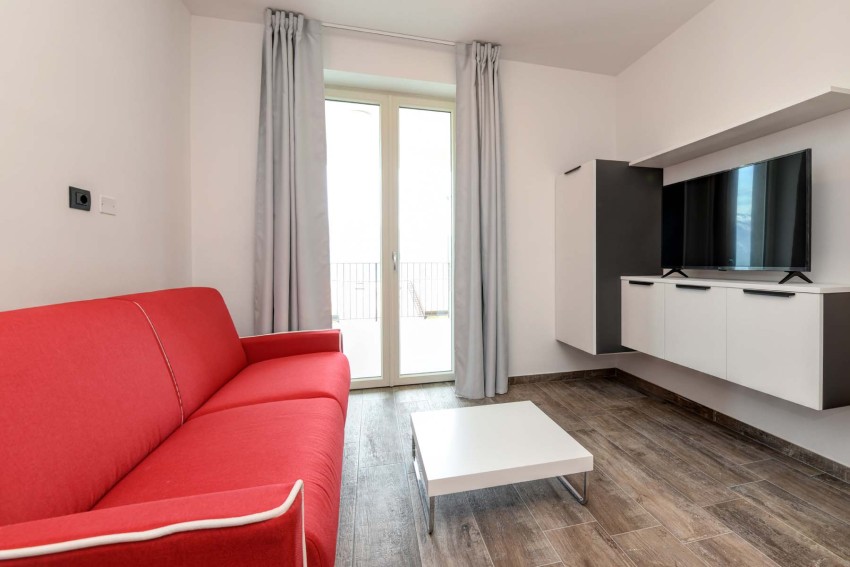Soggiorno moderno con divano rosso, TV a parete e tavolino, Lago di Garda.
