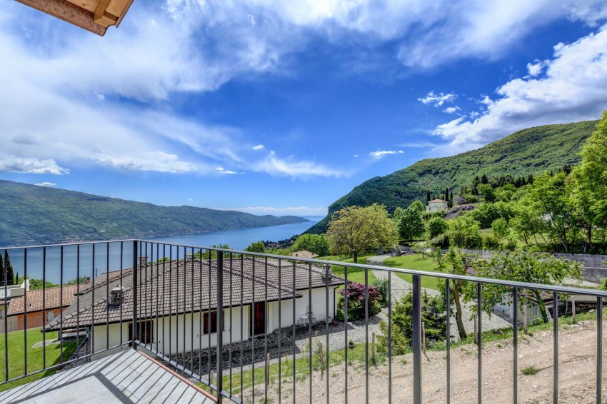 Vista dalla terrazza sul Lago di Garda con case, colline verdi e cielo azzurro.