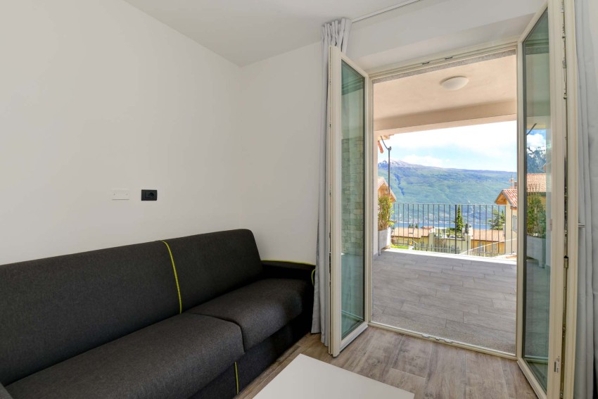 Helles Wohnzimmer mit Sofa und Balkon mit Blick auf den Gardasee und Berge