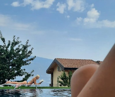 Woman reading on poolside lounger by a house and mountains at Lake Garda.