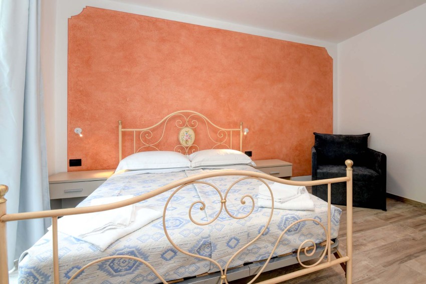Cozy bedroom with wrought-iron bed and orange wall near Lago di Garda.